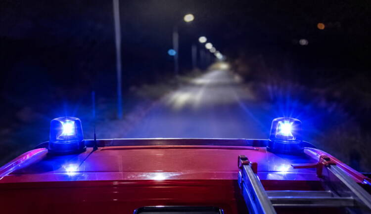 Luces azules encendidas sobre el techo de un camión de bomberos que circula de noche por una carretera arbolada.