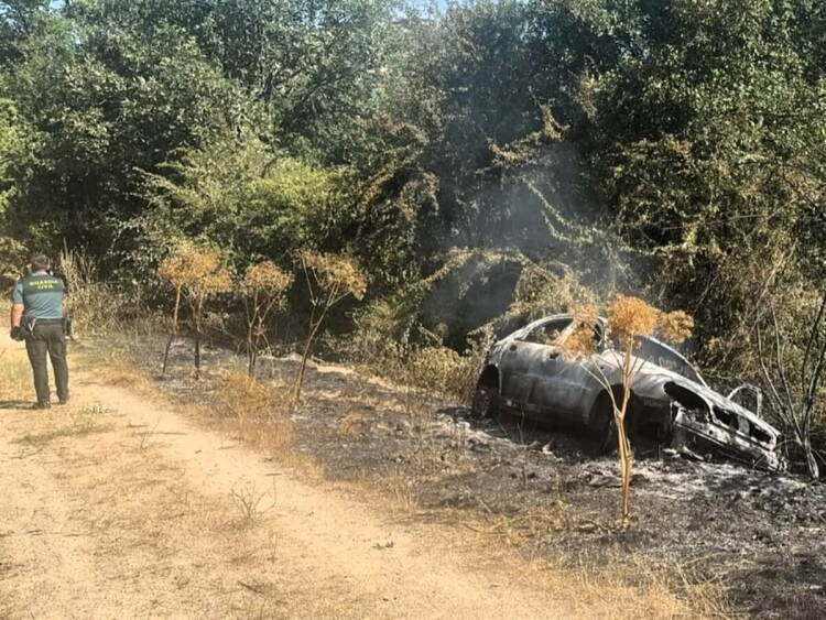 Turismo calcinado tras un accidente mortal en el Camino de los Prodigios, entre Miranda del Castañar y Villanueva del Conde (Salamanca), con un agente de la Guardia Civil inspeccionando la zona