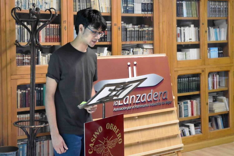 Joven premiado sostiene el diploma del certamen junto a una representante de La Lanzadera en la biblioteca