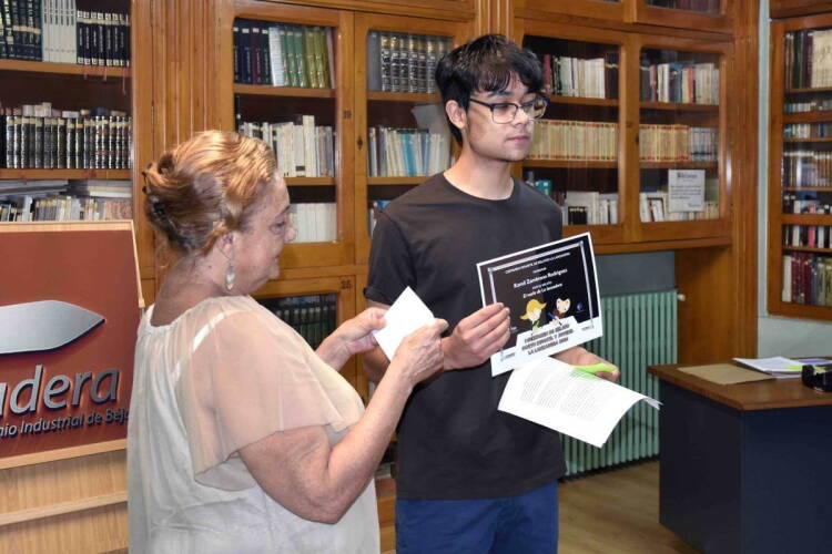 premiado sostiene el diploma del certamen junto a una representante de La Lanzadera en la biblioteca