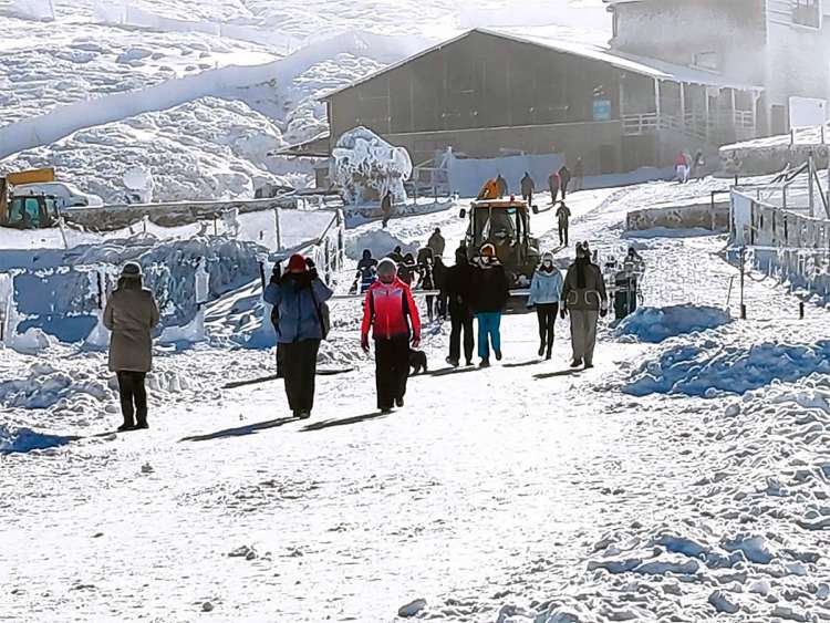 Montaña nevada con edificio al fondo y gente andando