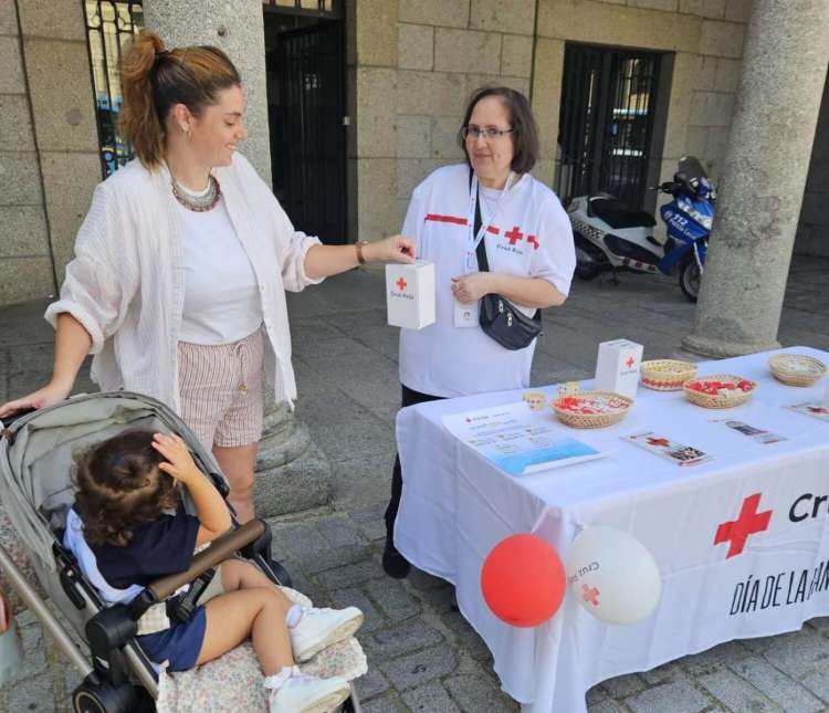 Una voluntaria de Cruz Roja recoge una donación durante el Día de la Banderita 2024 en Béjar, junto a una madre y su hija en carrito.
