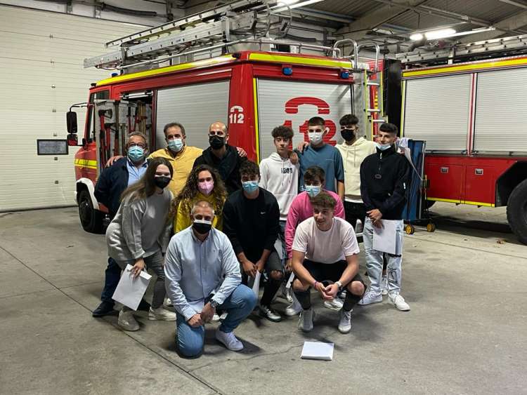 Varias personas con diplomas de la mano. Al fondo varios camiones de bomberos