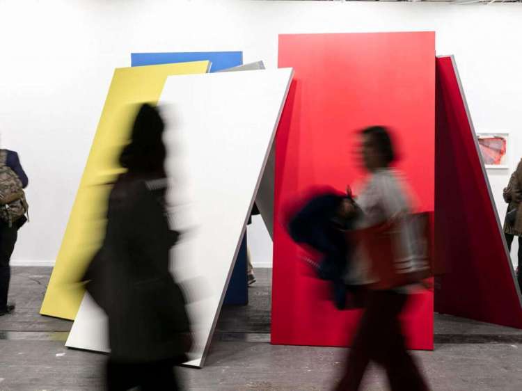 varias personas paseando delante de una obra formada por paneles de varios colores