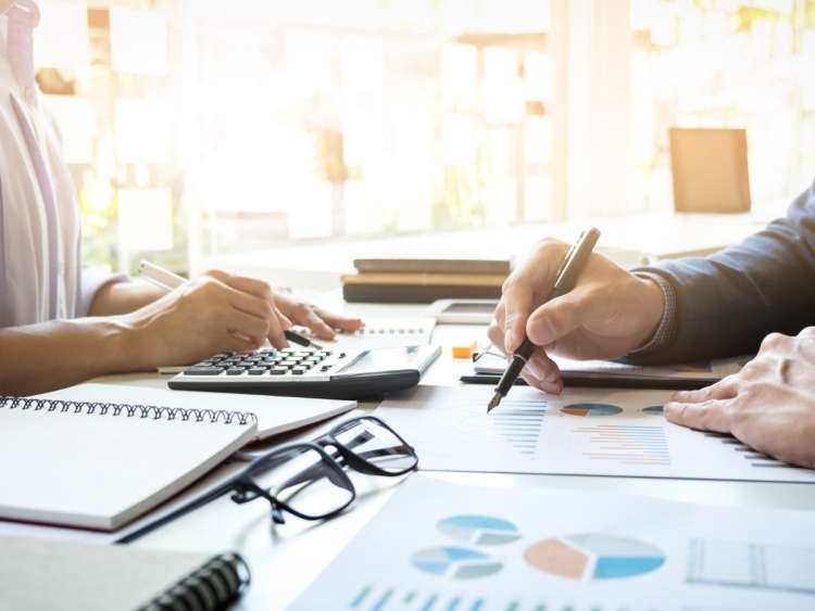 Mesa de oficina con papeles, gafas, cuadernos, bolis y varias manos