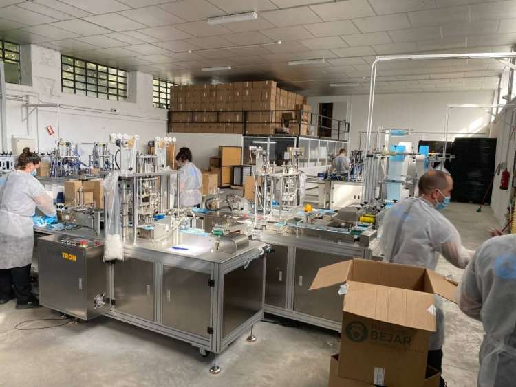 Varios operarios, entre maquinas, fabricando mascarillas