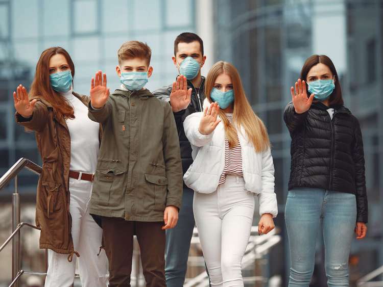 Personas usando mascarillas protectoras muestran señales de alto con las manos