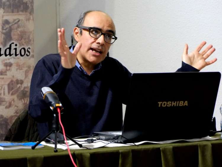 Persona gesticulando con las manos, sentada a una mesa con un portátil delante