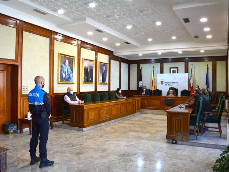 Sala grande con un policía de pie y varias personas sentadas