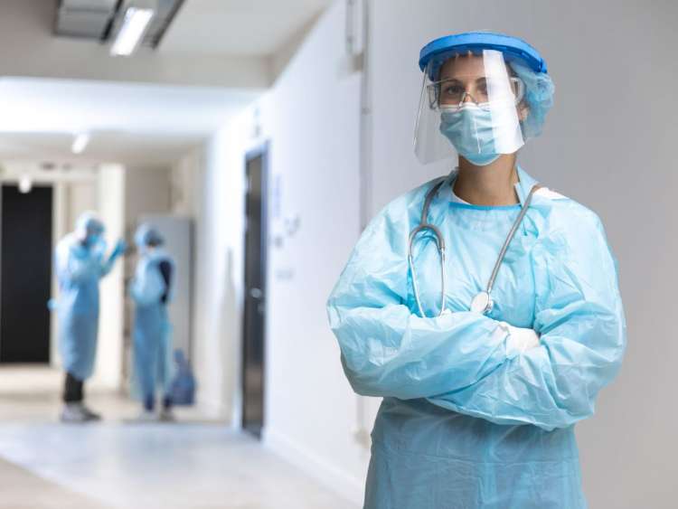 Sanitario en medio de un pasillo con traje EPI y dos sanitarios al fondo