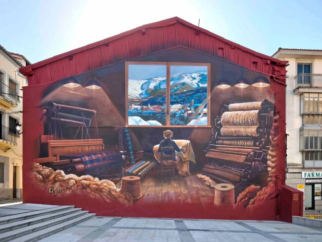 Mural dedicado a la tradición textil de Béjar con un telar, una hilandera y la Sierra de Béjar al fondo