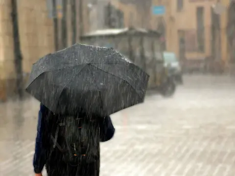Persona caminando bajo la lluvia intensa con un paraguas negro en una calle urbana.