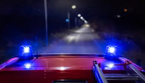 Luces azules encendidas sobre el techo de un camión de bomberos que circula de noche por una carretera arbolada.