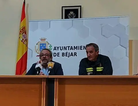 Dos personas sentadas en una mesa con microfonos