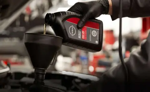 Mecánico vertiendo aceite de motor Nissan 0W-20 en un vehículo con la ayuda de un embudo.