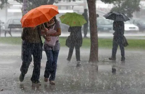 Varios jóvenes andando bajo la lluvia con paraguas