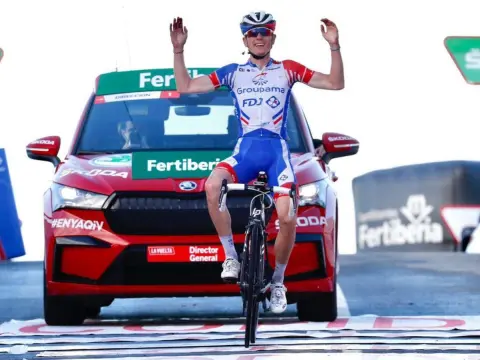 Ciclista con brazos en alto con coche detrás